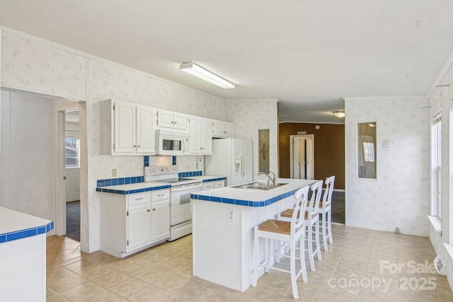 kitchen with sink, a breakfast bar area, white cabinetry, a center island with sink, and white appliances