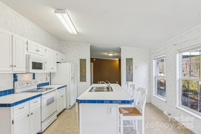 kitchen with sink, white cabinetry, a center island with sink, a kitchen breakfast bar, and white appliances