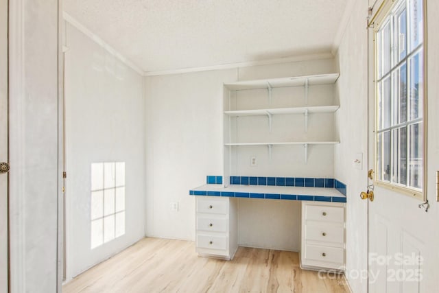 unfurnished office with ornamental molding, built in desk, light hardwood / wood-style floors, and a textured ceiling