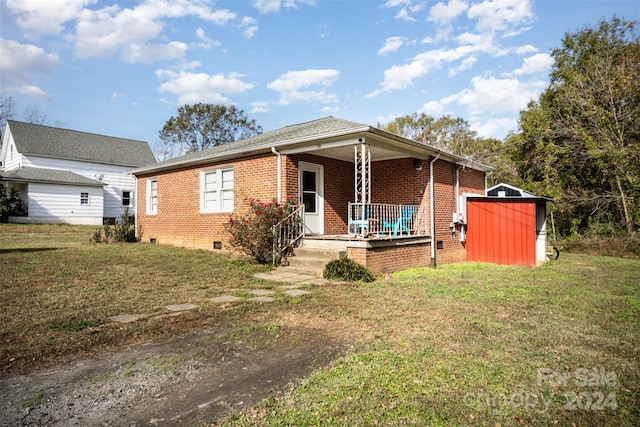 view of front of property featuring a storage unit, a porch, and a front lawn