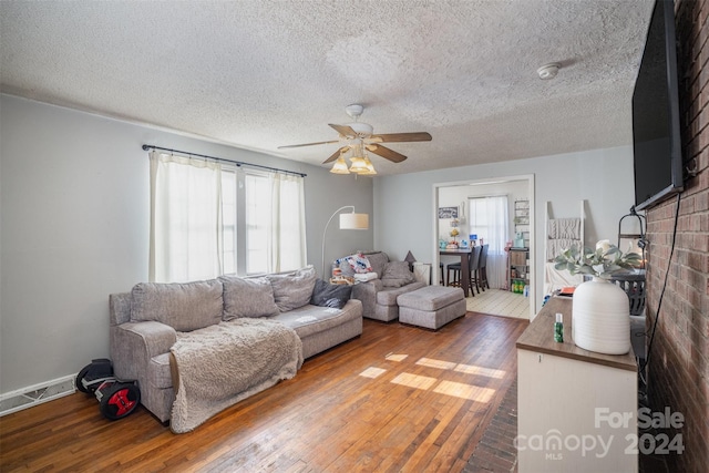 living room featuring hardwood / wood-style floors, a textured ceiling, a brick fireplace, and ceiling fan