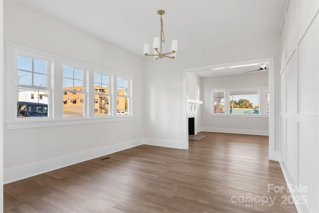 unfurnished dining area featuring a brick fireplace, dark hardwood / wood-style floors, and a notable chandelier