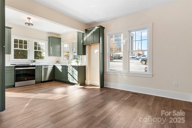 kitchen with green cabinets, stainless steel appliances, and light hardwood / wood-style flooring