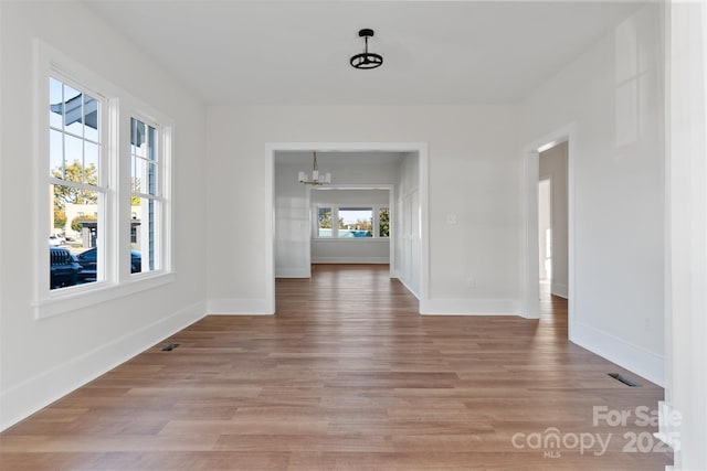 unfurnished dining area with light wood-type flooring, an inviting chandelier, baseboards, and visible vents