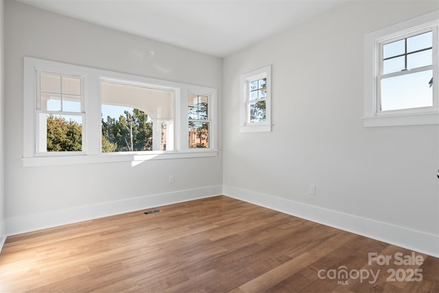 unfurnished room with wood finished floors, visible vents, and baseboards