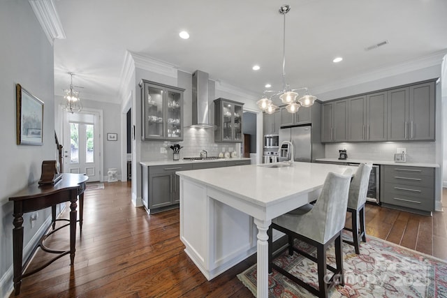 kitchen featuring a kitchen island with sink, hanging light fixtures, wall chimney exhaust hood, gray cabinets, and stainless steel appliances