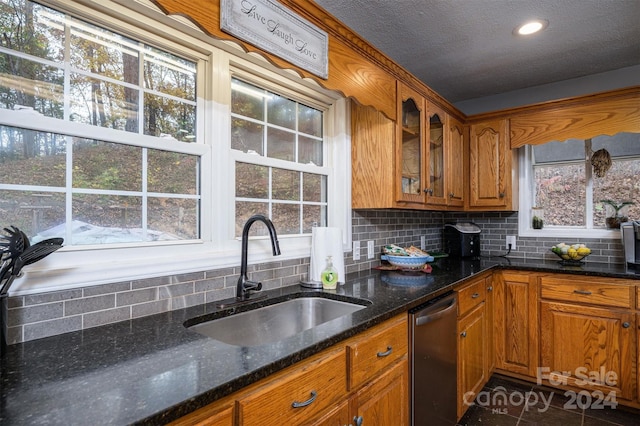 kitchen with sink, stainless steel dishwasher, dark tile patterned floors, backsplash, and dark stone countertops