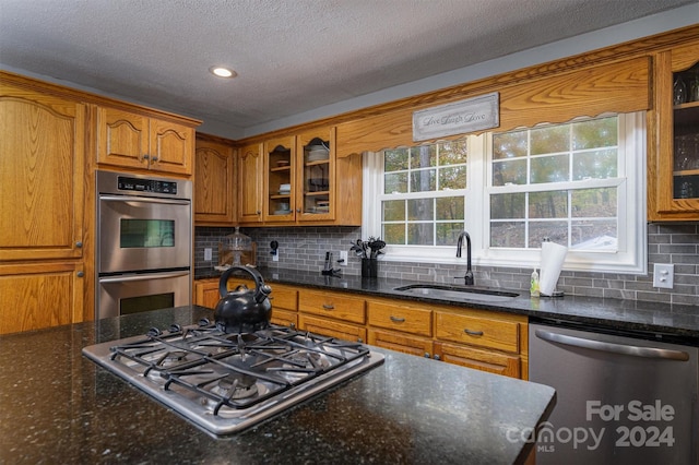 kitchen featuring appliances with stainless steel finishes, sink, dark stone countertops, and backsplash