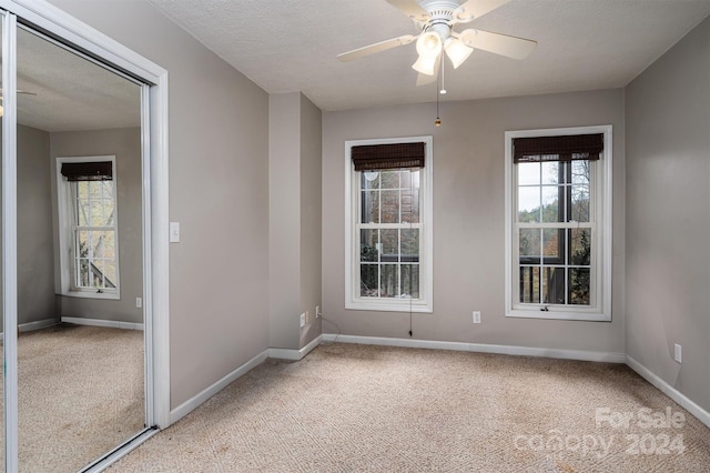 spare room with a textured ceiling, light carpet, and ceiling fan