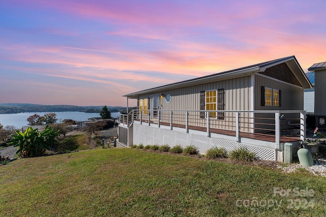 property exterior at dusk featuring a yard and a deck with water view