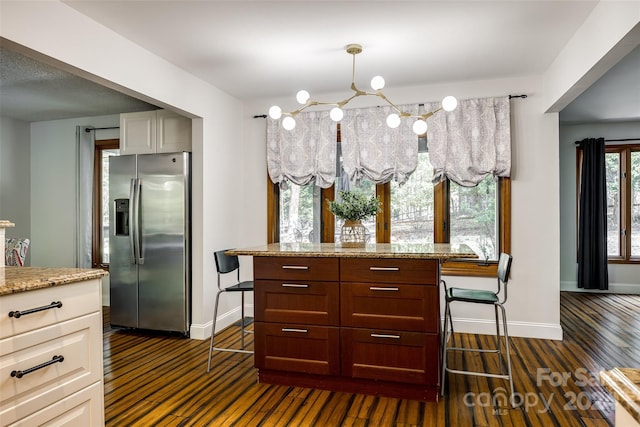 kitchen featuring light stone countertops, stainless steel fridge with ice dispenser, dark hardwood / wood-style flooring, and hanging light fixtures