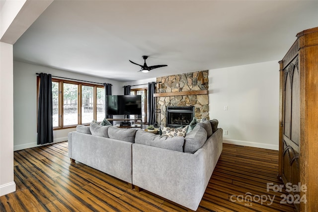 living room with ceiling fan, dark hardwood / wood-style floors, and a stone fireplace