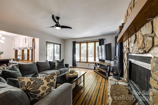 living room featuring dark hardwood / wood-style flooring, a stone fireplace, and ceiling fan