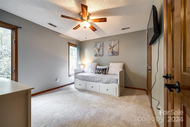 bedroom featuring ceiling fan, light colored carpet, and a textured ceiling