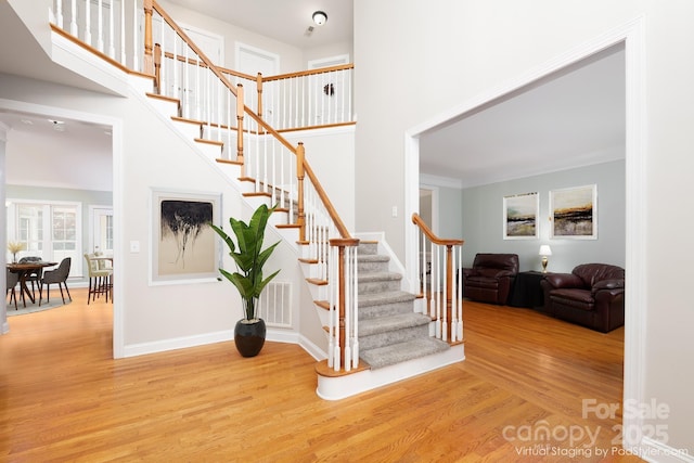 staircase with ornamental molding, a towering ceiling, and hardwood / wood-style floors