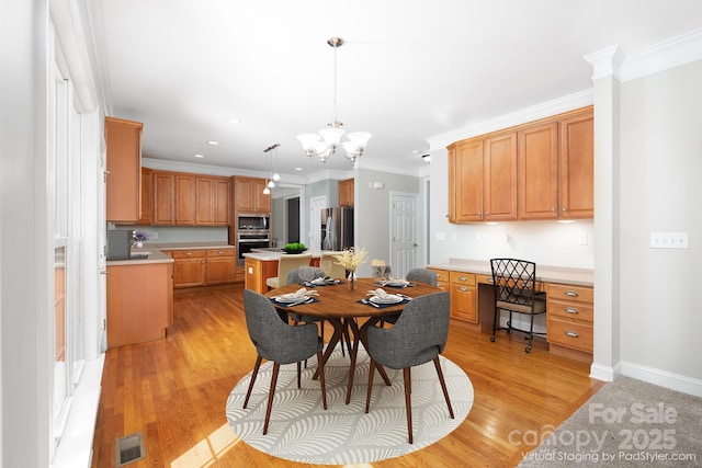 dining area with crown molding, a notable chandelier, built in desk, and light wood-type flooring