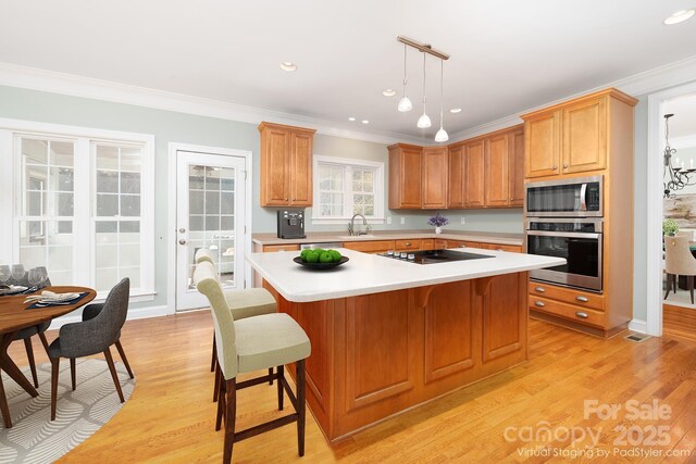 kitchen with sink, appliances with stainless steel finishes, a center island, ornamental molding, and decorative light fixtures