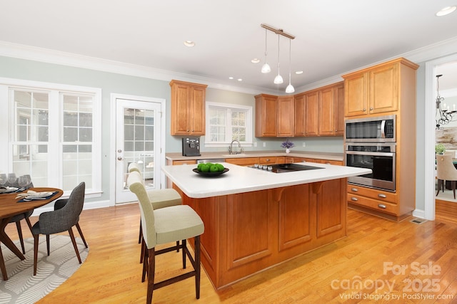 kitchen with sink, crown molding, appliances with stainless steel finishes, a center island, and decorative light fixtures