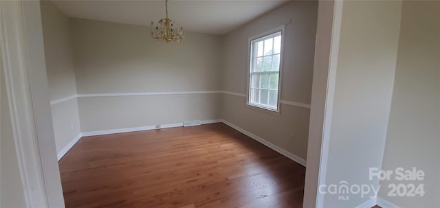 empty room featuring hardwood / wood-style flooring and an inviting chandelier