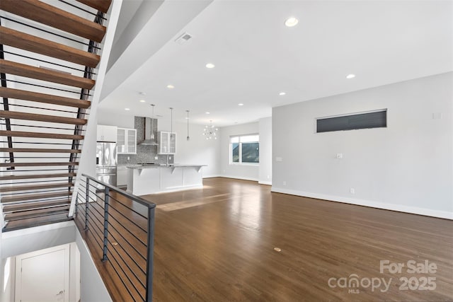 kitchen featuring backsplash, white cabinets, wall chimney range hood, a notable chandelier, and stainless steel refrigerator