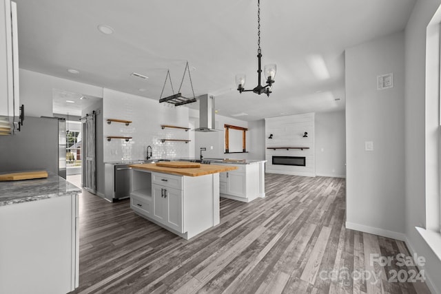 kitchen featuring hardwood / wood-style flooring, white cabinetry, range hood, a barn door, and wood counters