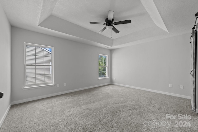 unfurnished room with a barn door, carpet flooring, ceiling fan, and a raised ceiling