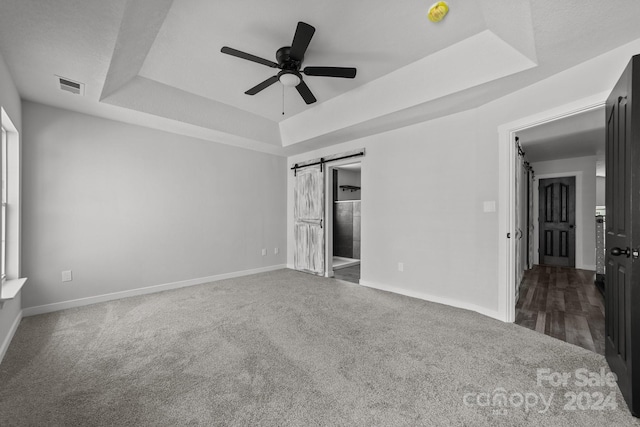 unfurnished bedroom featuring a tray ceiling, a barn door, ceiling fan, and ensuite bath