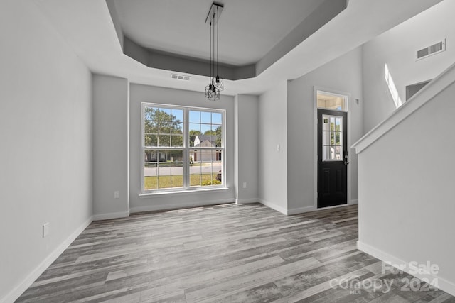 unfurnished dining area with light hardwood / wood-style flooring and a tray ceiling