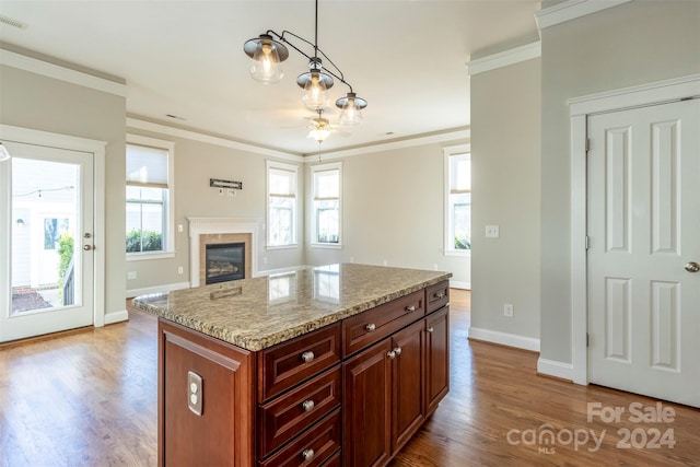 kitchen featuring light hardwood / wood-style floors, a center island, hanging light fixtures, ornamental molding, and light stone countertops