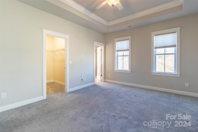 unfurnished bedroom with ceiling fan, a raised ceiling, crown molding, a walk in closet, and a closet