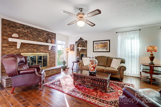 living room featuring a brick fireplace, a textured ceiling, hardwood / wood-style flooring, ceiling fan, and crown molding