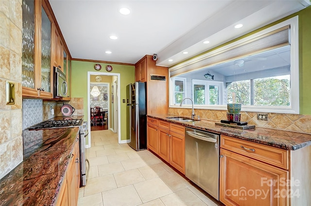 kitchen with dark stone counters, backsplash, appliances with stainless steel finishes, light tile patterned floors, and sink