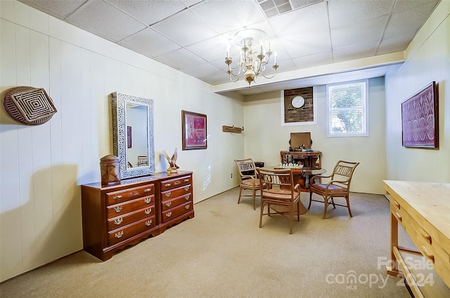 carpeted dining room featuring wooden walls, a drop ceiling, and an inviting chandelier