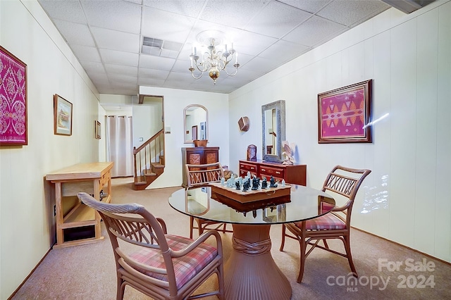 dining room with carpet flooring, a drop ceiling, and an inviting chandelier