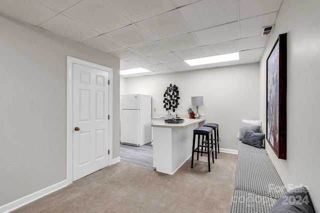 kitchen featuring a paneled ceiling, white fridge, light colored carpet, kitchen peninsula, and a breakfast bar area