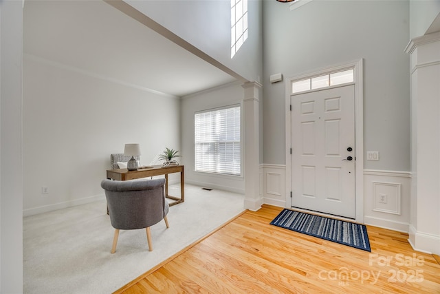 foyer with a wainscoted wall, decorative columns, visible vents, ornamental molding, and wood finished floors