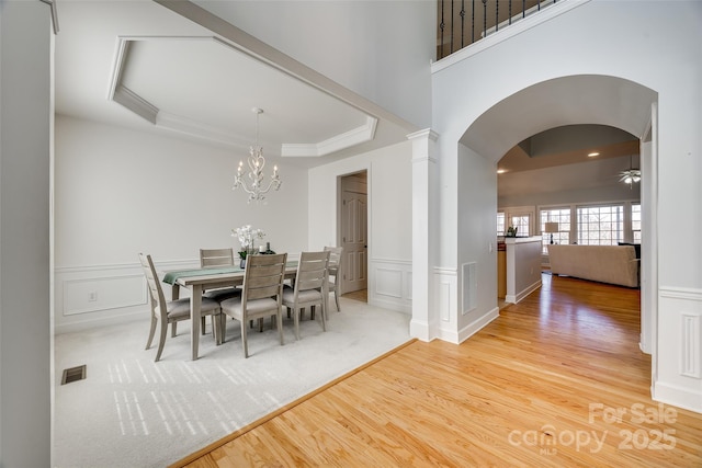 dining area with decorative columns, a raised ceiling, visible vents, a decorative wall, and wood finished floors