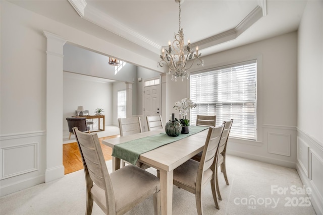 dining room featuring light carpet, wainscoting, a raised ceiling, and a decorative wall