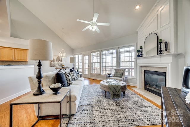 living area with a fireplace, ceiling fan, high vaulted ceiling, light wood-type flooring, and baseboards