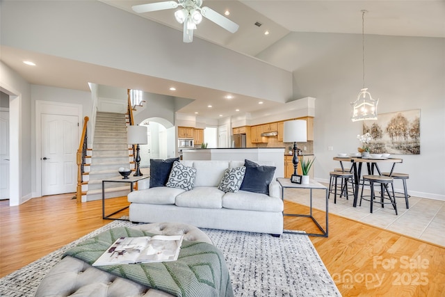 living room with arched walkways, high vaulted ceiling, baseboards, stairs, and light wood-type flooring