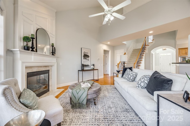 living area with arched walkways, a fireplace, stairway, light wood-type flooring, and baseboards