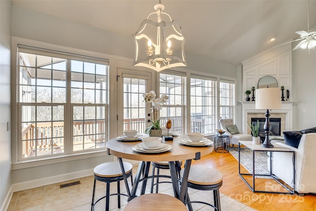 dining space featuring visible vents, baseboards, vaulted ceiling, a glass covered fireplace, and an inviting chandelier