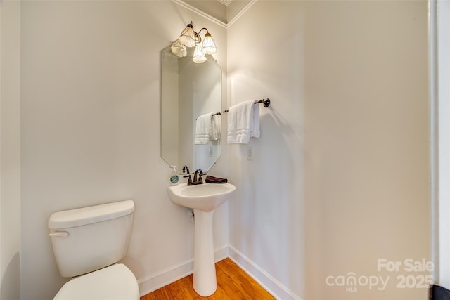 half bath with a sink, wood finished floors, toilet, and baseboards