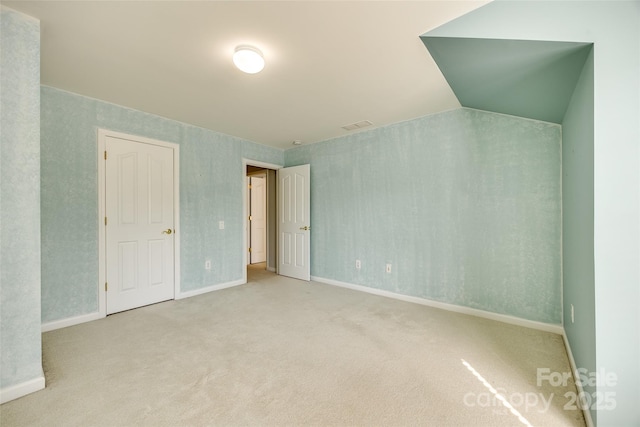 spare room with lofted ceiling, baseboards, visible vents, and light colored carpet