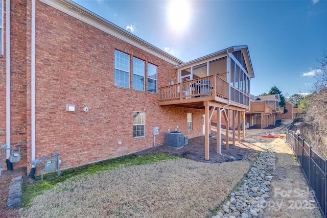 back of property featuring a sunroom, a fenced backyard, a deck, central AC, and brick siding