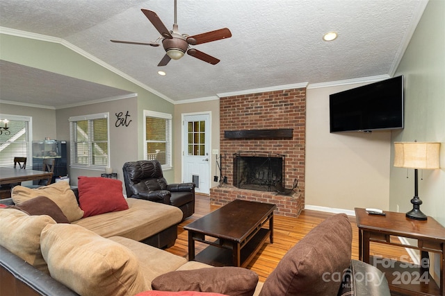 living room featuring a brick fireplace, vaulted ceiling, ceiling fan, crown molding, and light hardwood / wood-style flooring