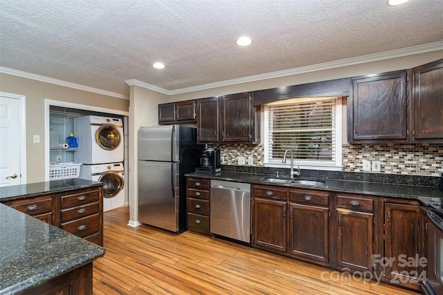 kitchen with stainless steel appliances, stacked washing maching and dryer, dark brown cabinetry, sink, and light wood-type flooring