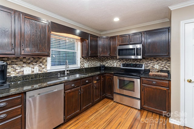 kitchen featuring ornamental molding, appliances with stainless steel finishes, sink, light hardwood / wood-style floors, and dark stone countertops