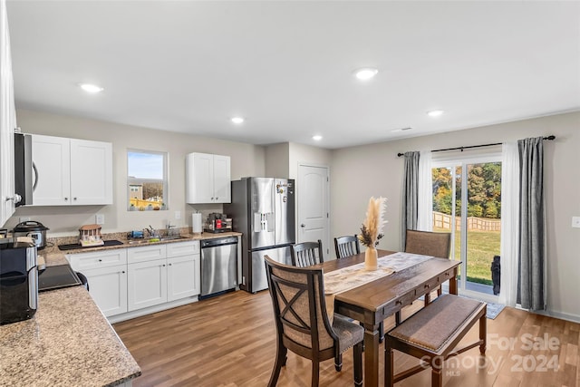 kitchen with light stone countertops, stainless steel appliances, sink, white cabinets, and hardwood / wood-style floors