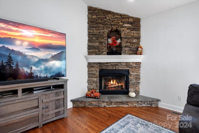 living room with hardwood / wood-style floors, vaulted ceiling, and a stone fireplace